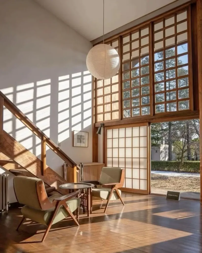 A sunlit Japandi room with large grid windows, wood floors, and two mid-century modern chairs.