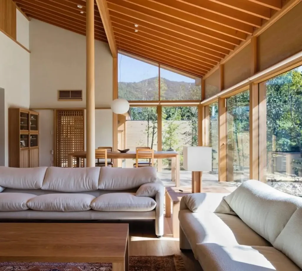 Modern Japanese style living room featuring a high wood ceiling and expansive glass walls overlooking a garden.