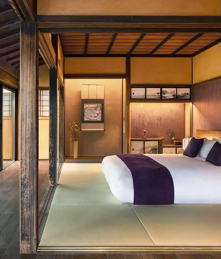 A traditional Japanese bedroom with dark wood beams, earthen walls, tatami floors, and a low bed.