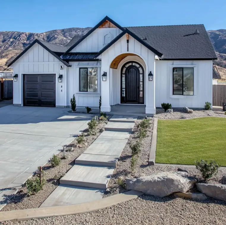 A white modern farmhouse ranch with a black garage door and an arched entryway.