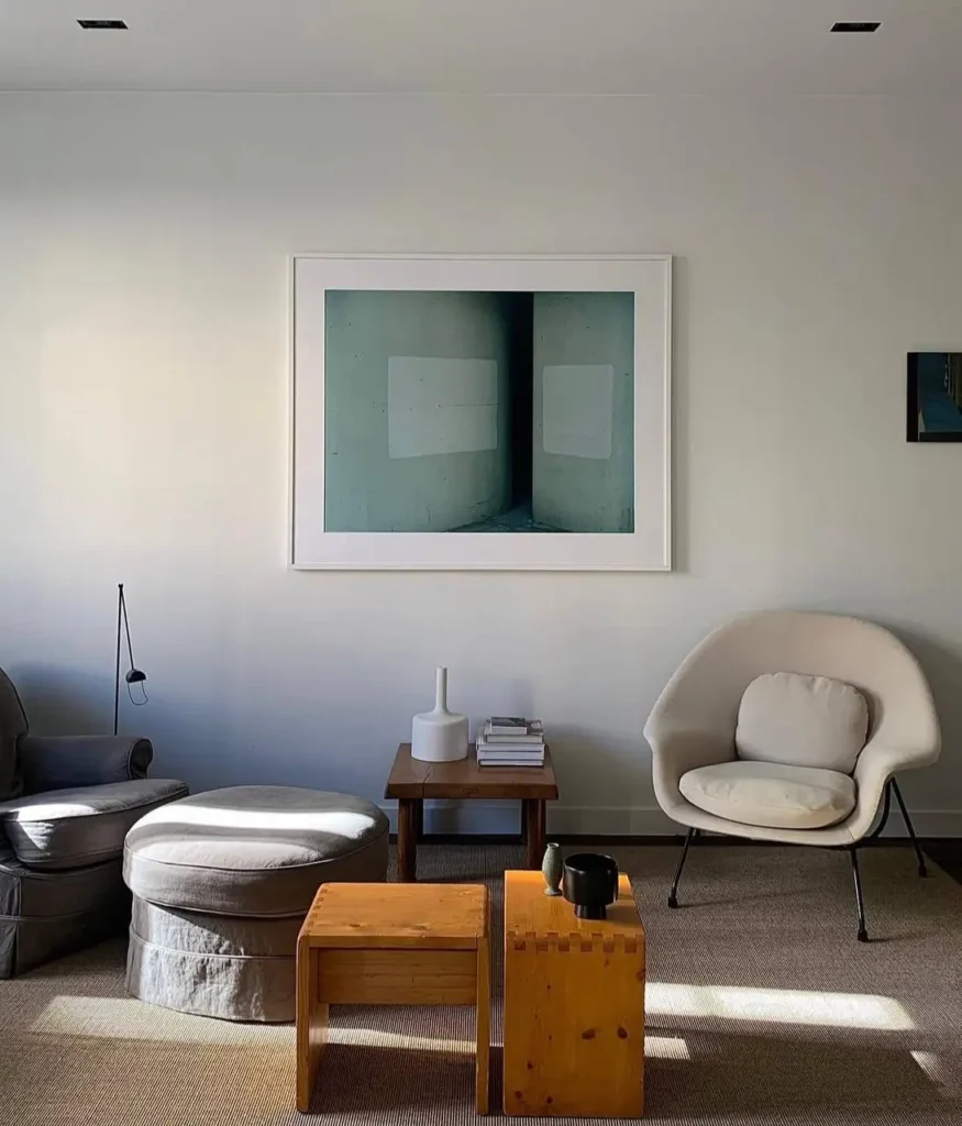 A minimalist living room corner with a modern chair, wooden stools, and large framed art.