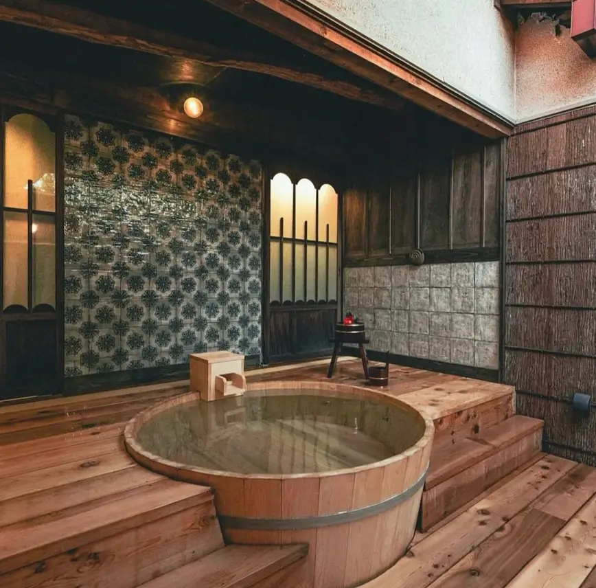 A traditional Japanese bathing room with a large circular wooden tub and decorative tiled walls.