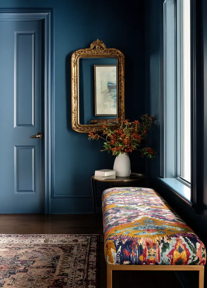 Modern Tudor Interior Design: A Definitive Guide 26 A modern, monochromatic Tudor entryway painted in a deep, moody blue, with a gold mirror and a colorful bench.