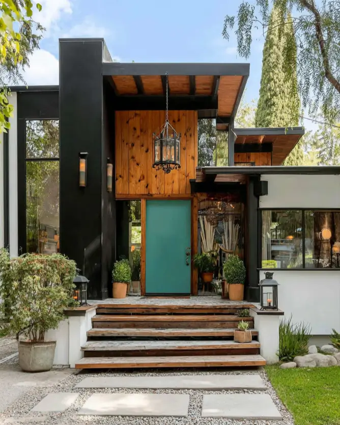 37 Mid Century Modern House Exteriors to Inspire Your Renovation 27 A mid century modern home exterior with a high-contrast entry, featuring a teal door, black-painted structure, and knotty wood siding.