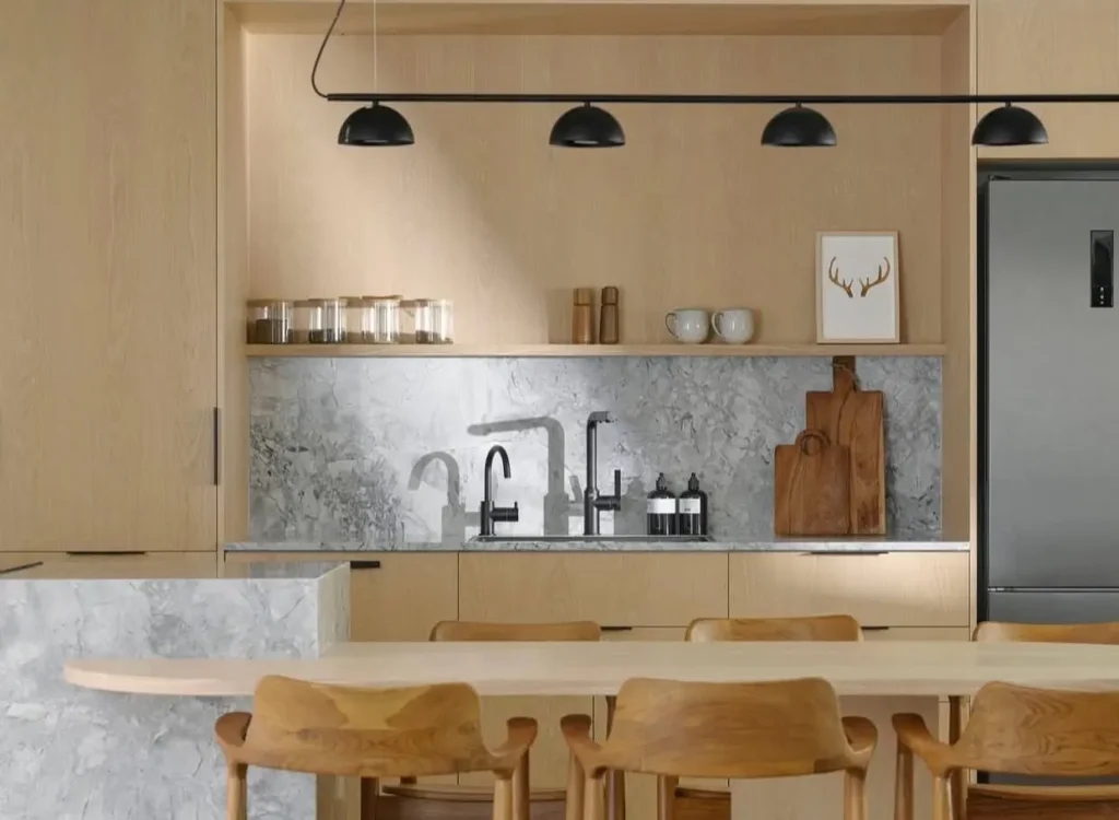 A Japanese kitchen design with light wood cabinets, a figured marble backsplash, and an integrated wood dining table.