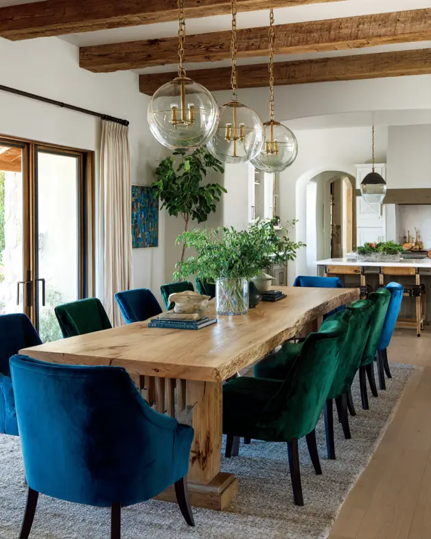 A modern ranch dining room with exposed wood beams, a live-edge table, and emerald velvet chairs.