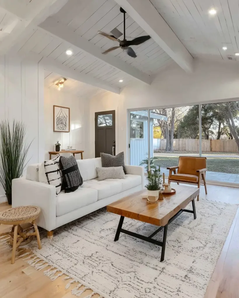A modern ranch style interior design living room with a white vaulted ceiling, white sofa, and a large glass door.