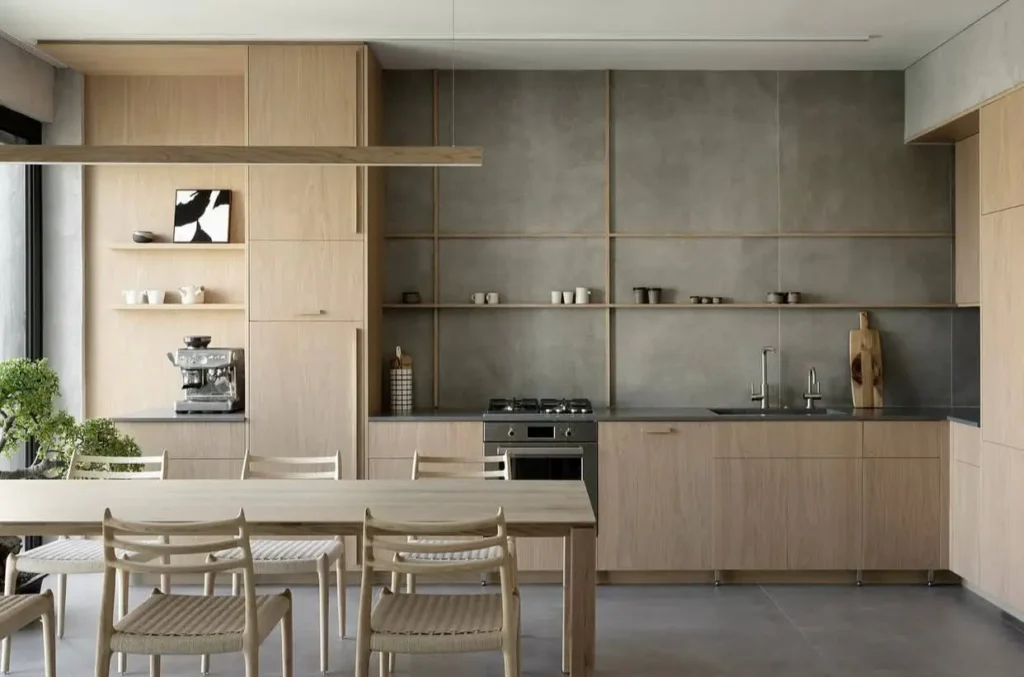 A Japanese kitchen design with light wood cabinets, a grey concrete-panel wall, and an integrated dining area.