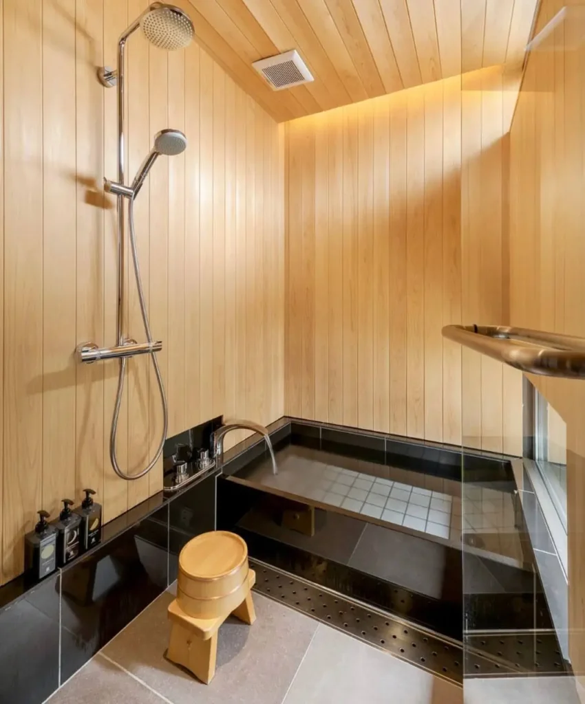26 Japanese Bathroom Design Ideas for a Serene Home Oasis 5 A small Japanese bathroom wet room with light wood walls, a black soaking tub, and a wooden stool.