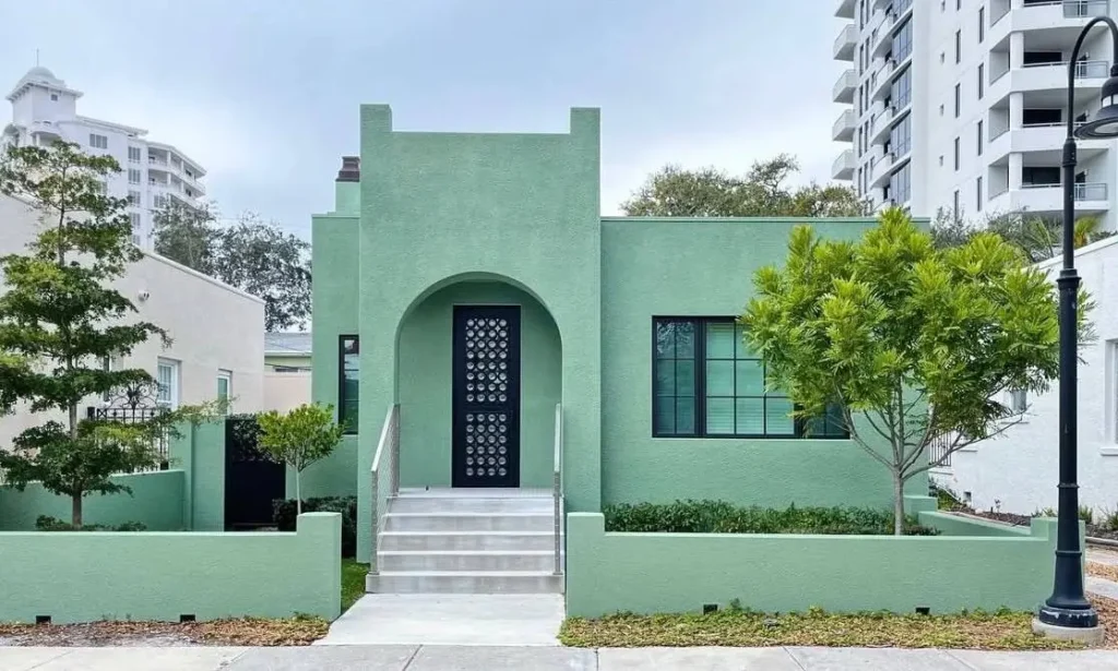 38 Small Mediterranean-Style Homes That Define Coastal Charm 5 Small Mediterranean home facade in modern mint stucco, defined by a central arched doorway and black metal grillwork.