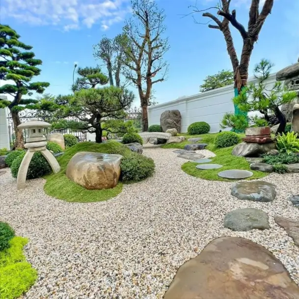 Complete Japanese zen garden with stone bridge, lantern, and sculptural pines on gravel.