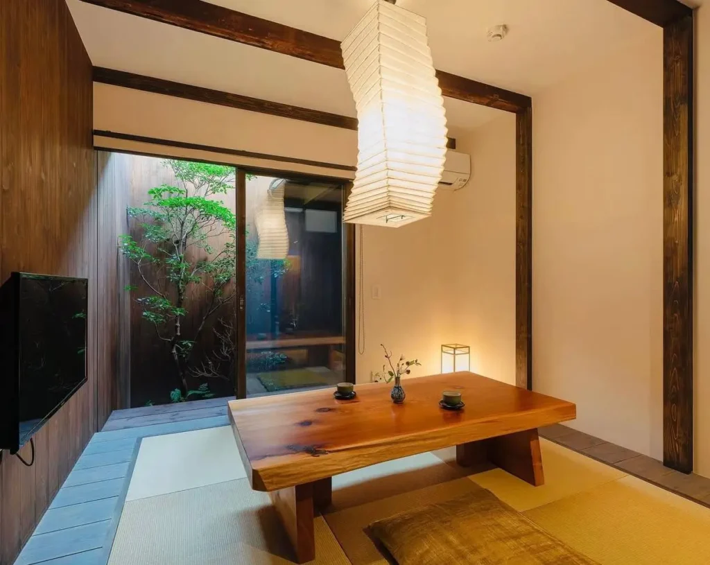Modern Japanese tatami room with a low live-edge table, paper lantern, and a courtyard view.