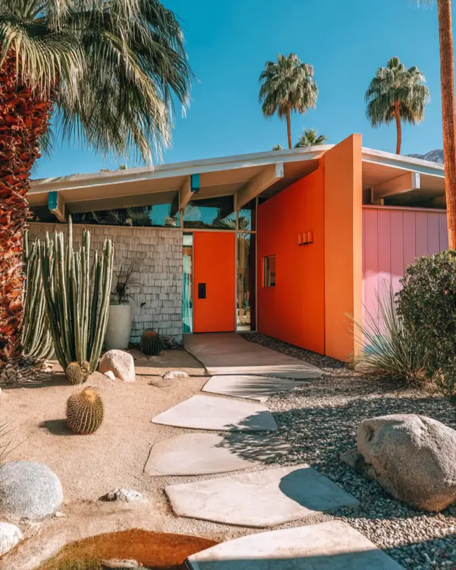 37 Mid Century Modern House Exteriors to Inspire Your Renovation 38 A mid century modern house exterior with bold orange and pink walls, wood shingles, and desert landscaping.