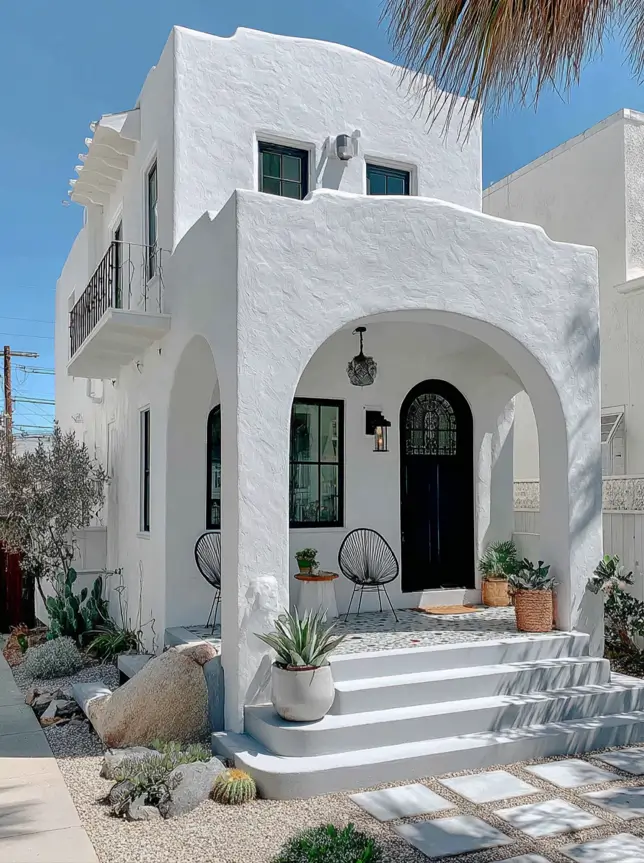 38 Small Mediterranean-Style Homes That Define Coastal Charm 38 Coastal minimalist small Mediterranean home with white textured stucco, large arches, and a low-maintenance desert landscape.