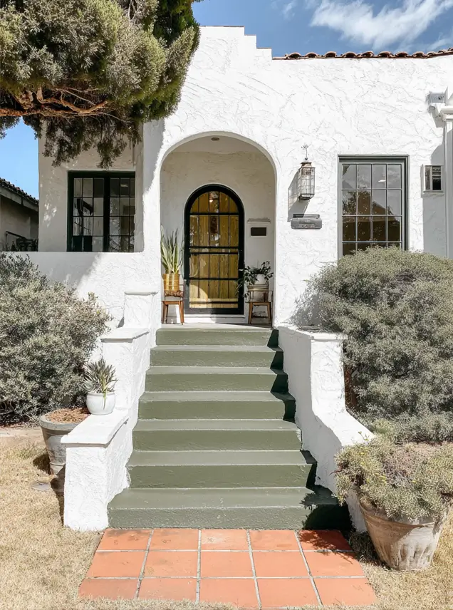 38 Small Mediterranean-Style Homes That Define Coastal Charm 6 Textured white small Mediterranean home bungalow with dark green painted steps and a black iron arched entry door.
