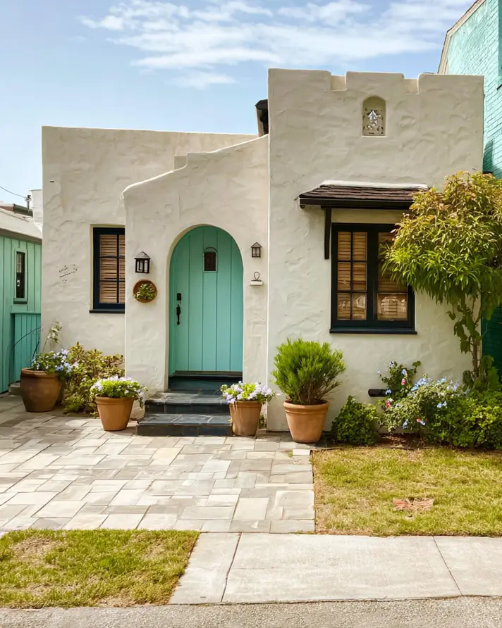 38 Small Mediterranean-Style Homes That Define Coastal Charm 7 Cream stucco small Mediterranean-style home with a vibrant teal arched door and dark window trim.