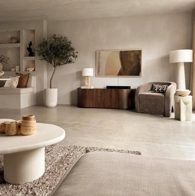A Japandi living room with textured neutral walls, a concrete floor, and curved, earthy furniture.