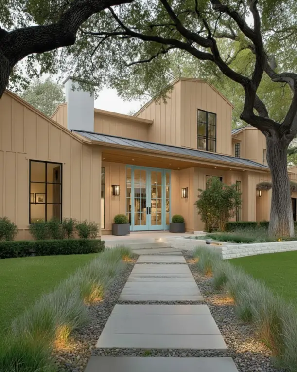 A modern farmhouse ranch home with warm tan siding, a light blue door, and an illuminated walkway.