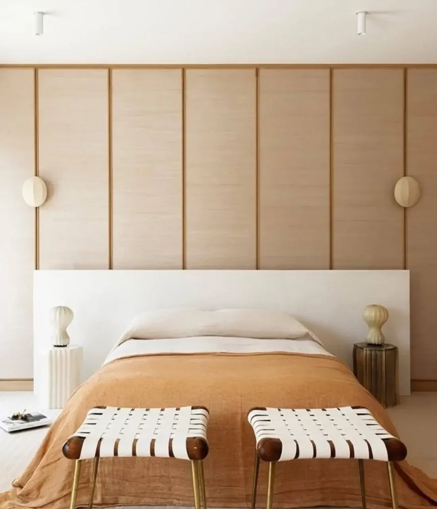 A modern Japanese-inspired bedroom with a light wood paneled wall, a white headboard, and a terracotta-colored blanket.