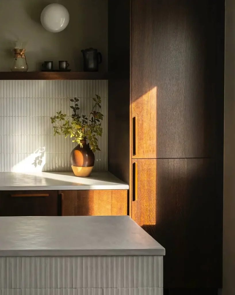 A texture-rich Japanese inspired kitchen with dark wood cabinets, a fluted island, and a vertical tile backsplash.