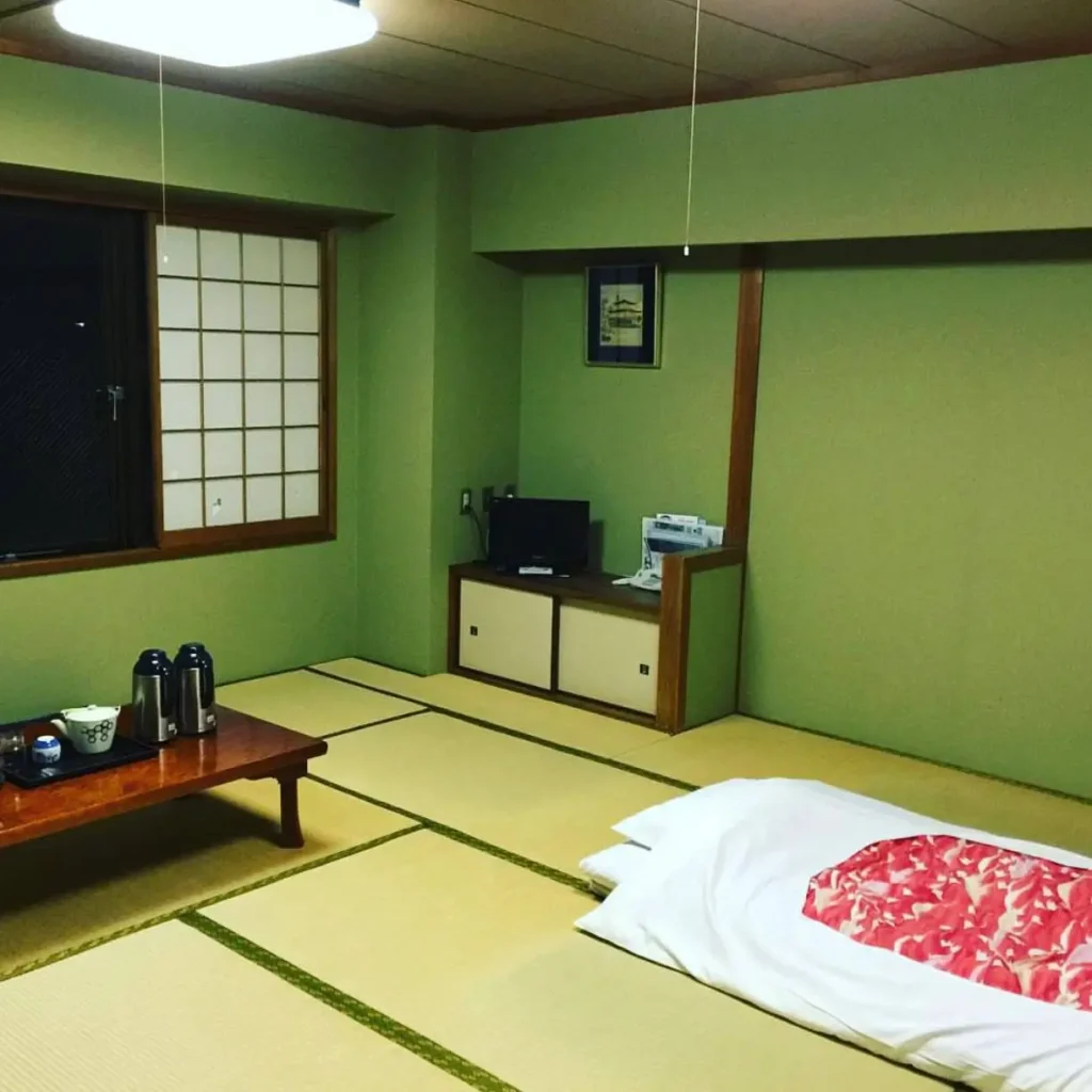 A traditional Japanese bedroom with green walls, tatami flooring, a low tea table, and a futon on the floor.