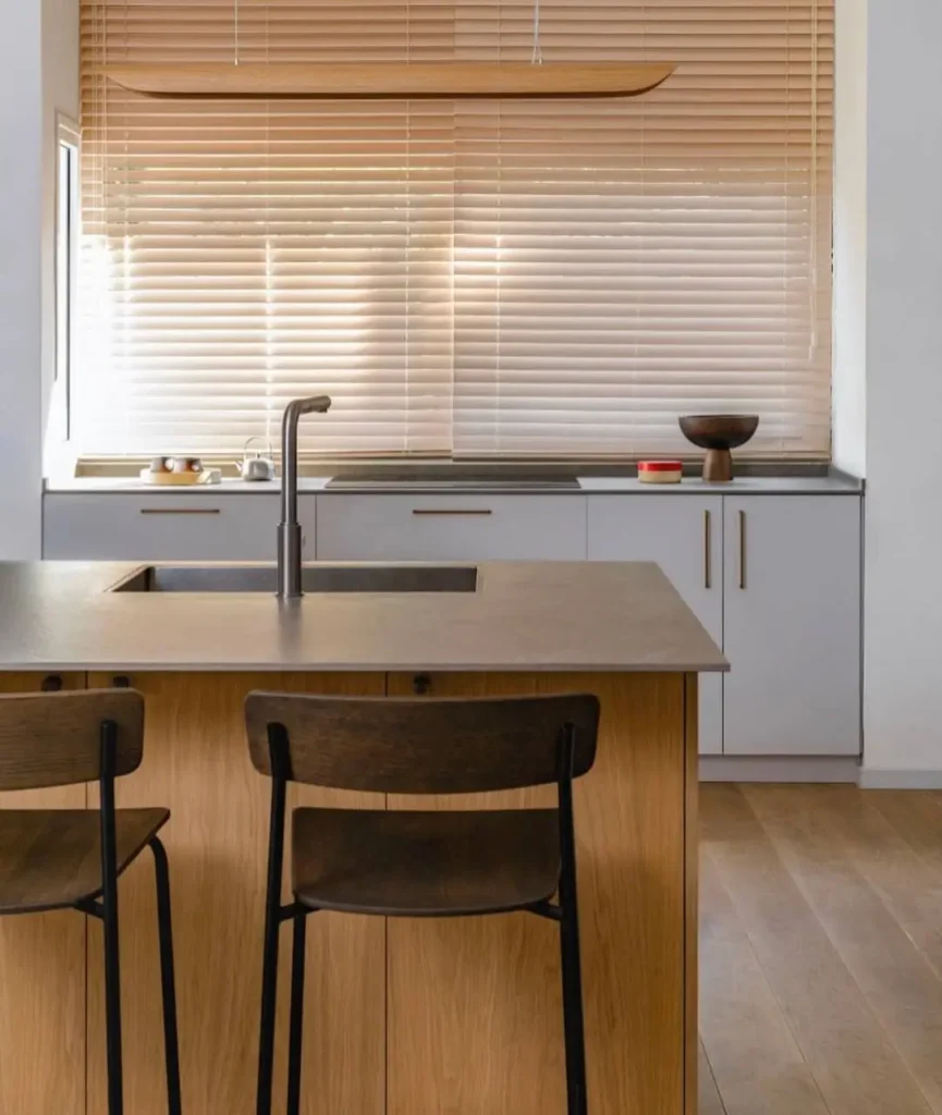 A Japanese inspired kitchen with a wood island, grey cabinets, and wooden blinds filtering light.