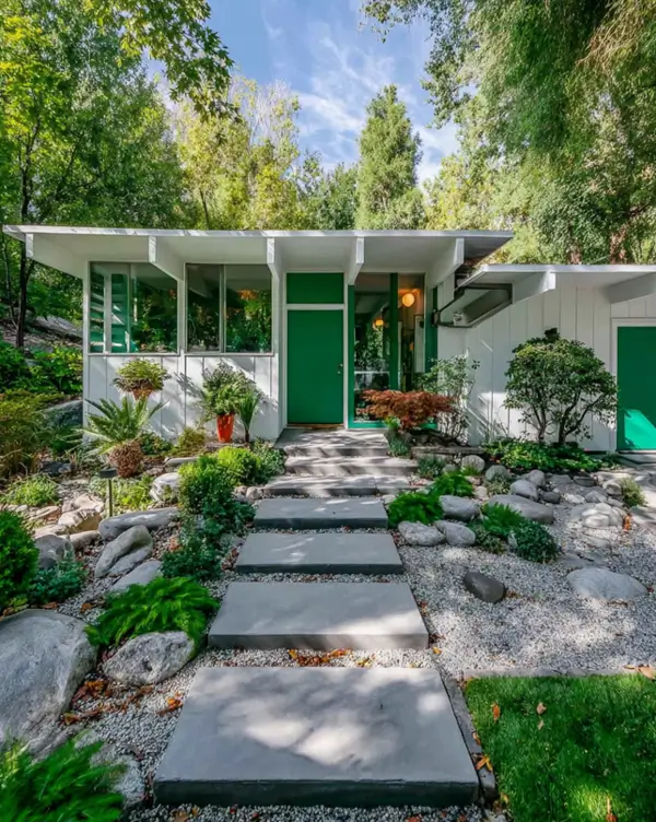 37 Mid Century Modern House Exteriors to Inspire Your Renovation 11 A white mid-century modern house exterior with vivid green doors, set in a lush, wooded landscape with a stone path.