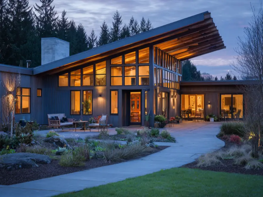 A sprawling modern ranch home at dusk with a dramatic wood-lined angled roof and a glowing interior.