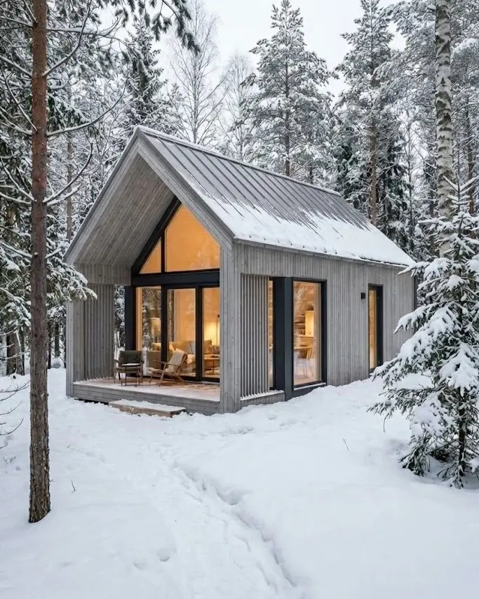 33 Small Scandinavian House Ideas That Prove Less Is More 21 Weathered winter cabin with silver-grey larch siding and a deep roof overhang in snowy woods.