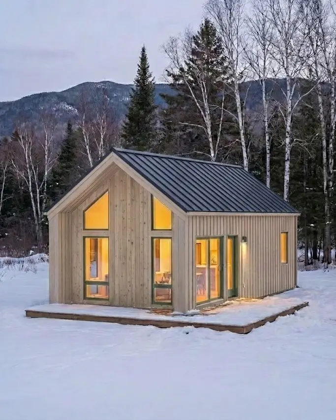 33 Small Scandinavian House Ideas That Prove Less Is More 23 Natural timber haven with vertical siding and large gable windows glowing in a winter landscape.