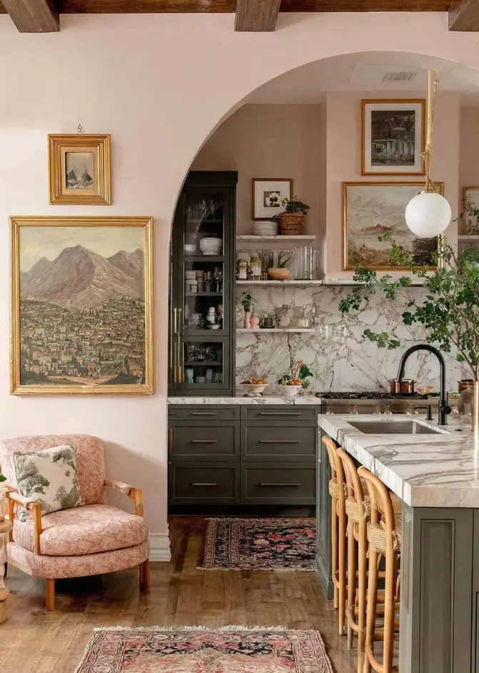 34 Modern Tudor Kitchen Ideas: Old-World Charm, New Appeal 29 Kitchen featuring soft pink walls, a large gold-framed painting, an arched doorway, and woven island stools.
