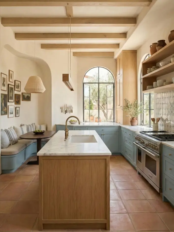 30 Mediterranean Kitchen Ideas for a Warm, Coastal Escape 17 Mediterranean kitchen idea featuring light blue cabinets, exposed wood ceiling beams, a marble-topped wood island, and a cozy corner banquette.