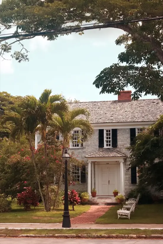 45 Colonial House Design Ideas for a Timeless Exterior 28 Island Colonial cottage with weathered shake shingle siding, white double front doors, black shutters, and tropical garden