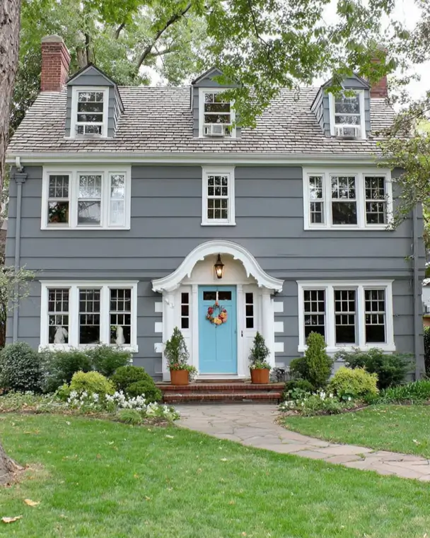 45 Colonial House Design Ideas for a Timeless Exterior 42 Slate gray painted Colonial home with sky blue front door, curved bonnet entry hood, white trim, three small dormers, and twin brick chimneys