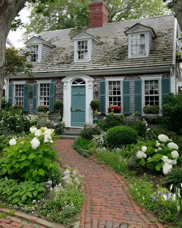 27 Cape Cod Style House Ideas for a Timeless New England Exterior 20 Weathered shake cottage with teal louvered shutters, three dormers, teal front door, brick path, hydrangeas, and geranium window boxes