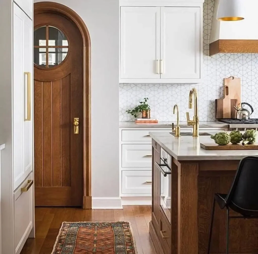 Colonial Style Kitchen: 26 Timeless Ideas, Cabinets & Designs 5 Modern colonial kitchen with an arched wood plank door, white cabinets, a marble island, and brass fixtures