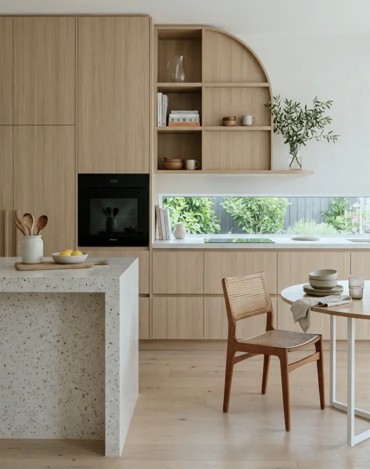 Japandi Kitchen: The Calm, Warm Look I Keep Coming Back To 5 Light oak kitchen with arched open shelving, a terrazzo island, and a cane dining chair
