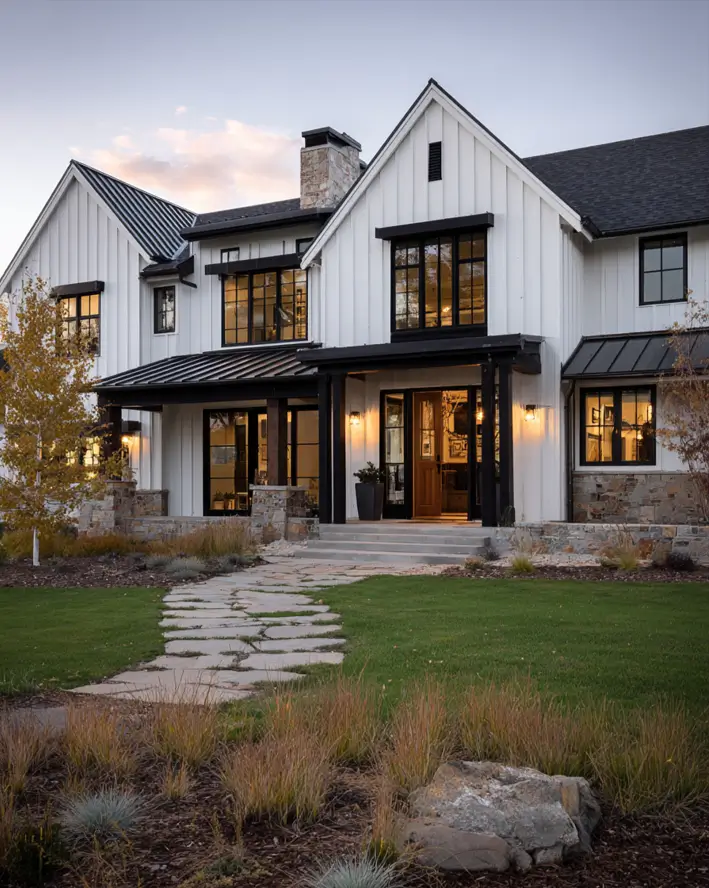 White Farmhouse with Stone Exterior: 29 Ideas That Feel Warm, Not Cold 16 Stone post bases and a low stone accent wall grounding a white farmhouse porch at dusk