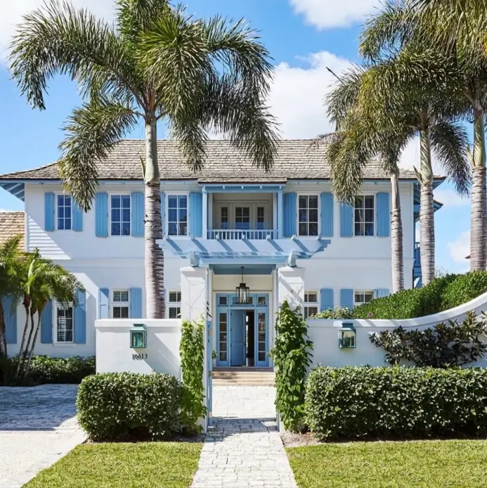 33 Blue and White Cottage Ideas That Always Feel Fresh 20 blue and white cottage exterior with sky-blue shutters, blue front door, and white stucco walls framed by palm trees