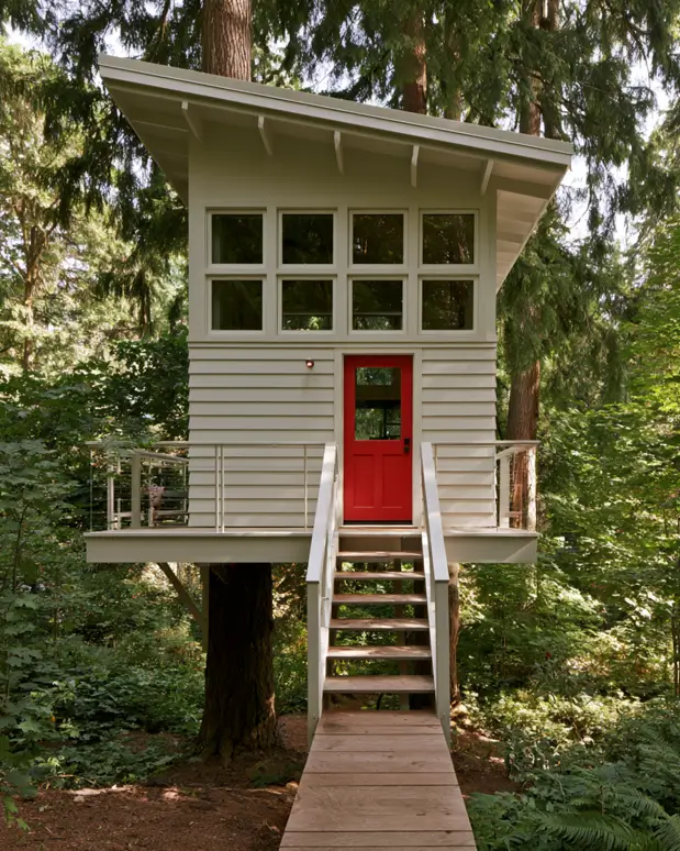 55 Treehouse Design Ideas, From Backyard Platforms to Canopy Cabins 21 Small treehouse ideas with painted lap siding, a red door, cable deck railings and an open timber stair