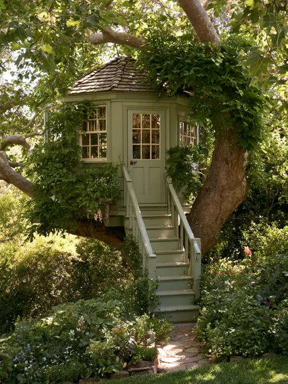 55 Treehouse Design Ideas, From Backyard Platforms to Canopy Cabins 23 Small treehouse ideas with sage green painted siding, white sash windows and climbing greenery over a garden stair