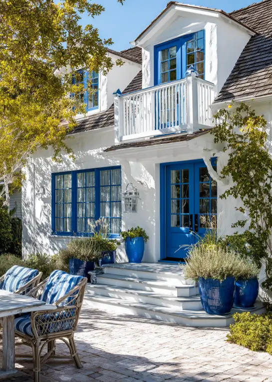 33 Blue and White Cottage Ideas That Always Feel Fresh 29 white and blue cottage exterior with white stucco, cobalt-blue French doors, blue window frames, and cobalt glazed planters