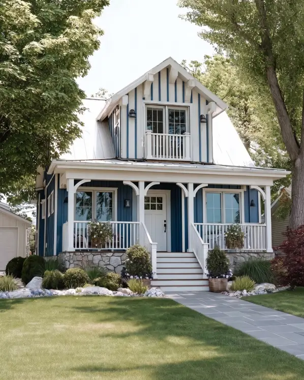 33 Blue and White Cottage Ideas That Always Feel Fresh 34 blue and white cottage exterior with blue board-and-batten siding, gambrel roof, stone base, white wraparound porch, and upper balcony