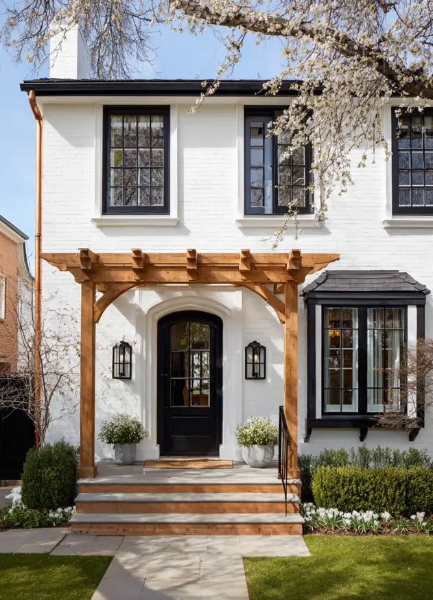 47 White Houses With Black Trim and Wood Accents We Love 7 Honey oak timber arbor over a black arched front door on white painted brick