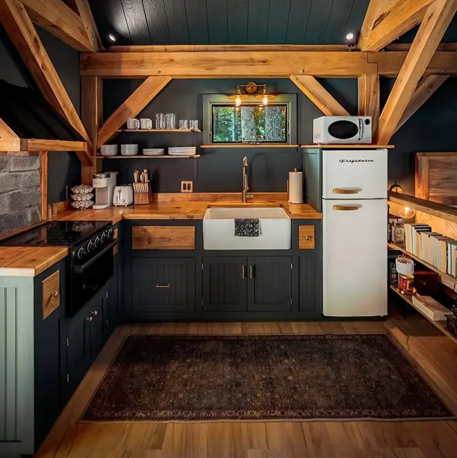 55 Treehouse Design Ideas, From Backyard Platforms to Canopy Cabins 54 Small treehouse ideas showing a compact galley kitchen with dark cabinets, timber worktops and a trunk-framing window