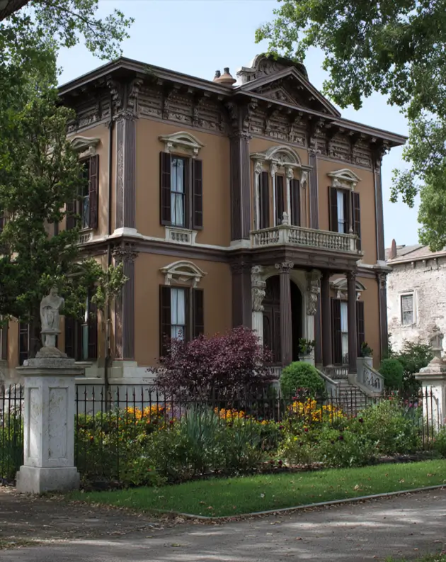 Italianate Style House: 33 Ideas and the Details That Give One Away 8 Italianate style house in warm tan with a centered pediment and a deep carved frieze between paired brackets