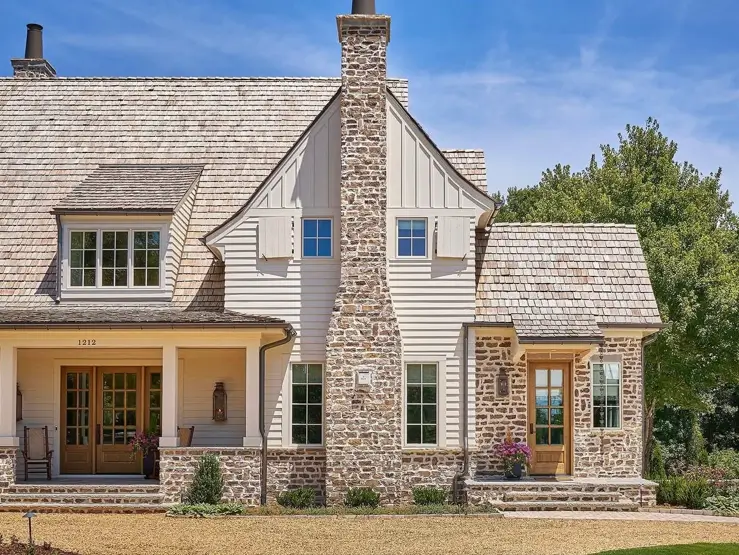 White Farmhouse with Stone Exterior: 29 Ideas That Feel Warm, Not Cold 2 White farmhouse with stone exterior with a stacked fieldstone chimney rising between cream gables under a cedar shake roof
