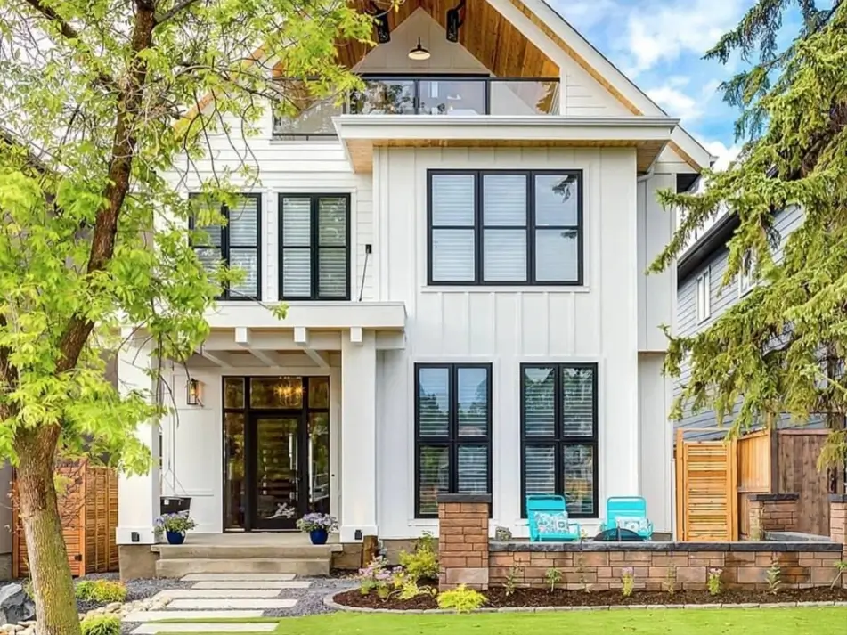 47 White Houses With Black Trim and Wood Accents We Love 2 White house with black trim and wood accents featuring a cedar gable, black-framed windows, and a timber privacy fence