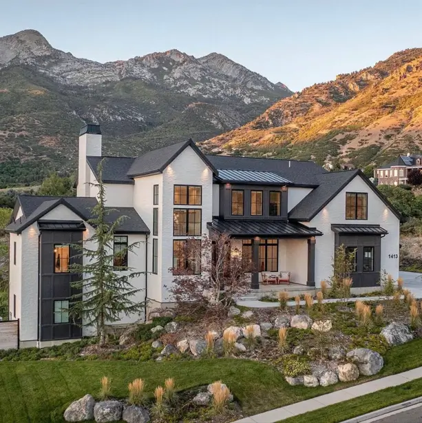 Hillside House Design: 38 Ideas for Building With the Slope 3 white painted brick hillside house design with black-framed windows and a mountain backdrop at dusk