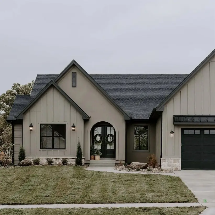 Taupe House With Black Trim: 28 Ideas + Best Paint Colors 15 Taupe house with black trim on greige board-and-batten with an arched black door and a stone base
